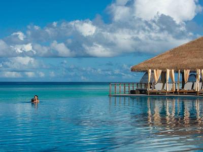 Endloser Pool am Meer mit blauem Himmel, Wolken und einer überdachten Terrasse am rechten Rand.