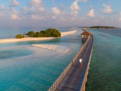Langer Steg führt über türkisfarbenes Wasser zu kleinen, grünen Inseln unter blauem Himmel mit weißen Wolken.