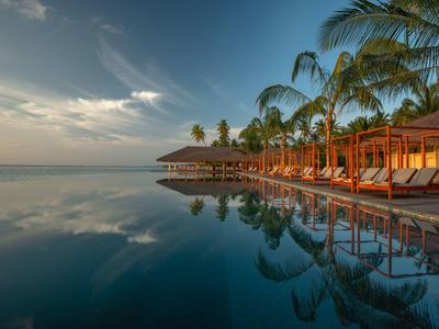 Luxushotel mit Pool, Palmen und Liegestühlen am ruhigen Meer bei Sonnenuntergang.