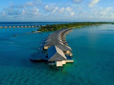 Luftaufnahme von Wasserbungalows, die sich entlang einer geschwungenen Landzunge im türkisfarbenen Meer erstrecken.