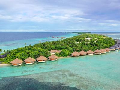 Grüne Insel mit Palmen und Holzhütten am türkisblauen Meer unter bewölktem Himmel.