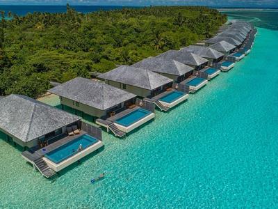 Reihe von Bungalows mit Pools über türkisblauem Wasser nahe einer grünen Insel.