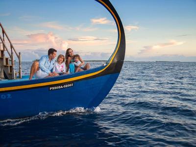 Drei Personen sitzen vorne auf einem blauen Boot bei ruhigem Meer und sonnigem Himmel.