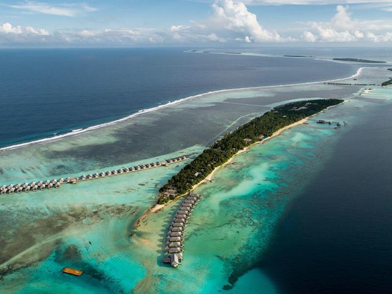 Langer tropischer Inselstreifen mit Palmen, Sandstrand und über Wasser gebauten Bungalows im Meer.