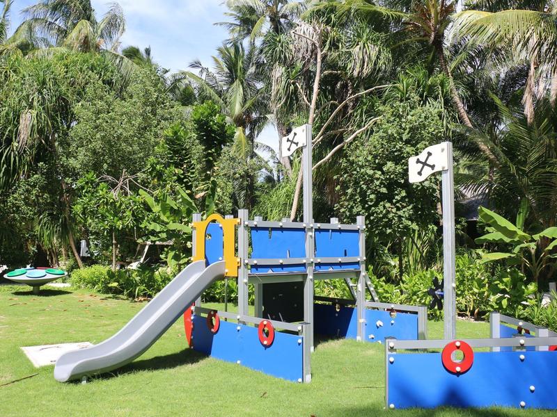 Bunter Kinderspielplatz mit Rutsche, Segel und Mast auf grünem Rasen im Park.