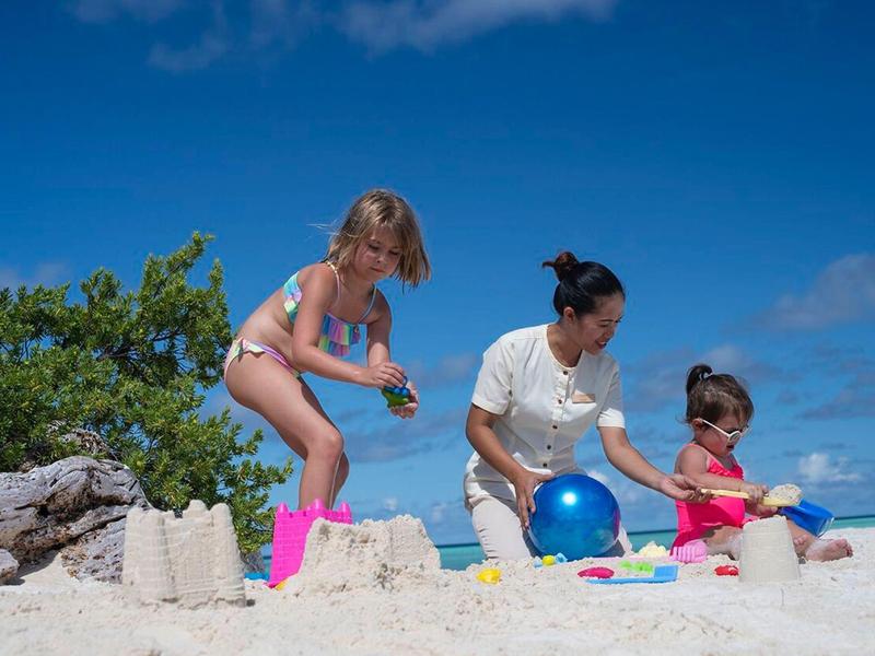 Drei Personen bauen Sandburgen am Strand bei klarem Himmel und blauem Ball.