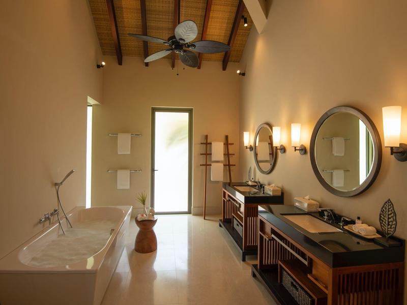 Geräumiges Badezimmer mit freistehender Badewanne, zwei Waschbecken, runden Spiegeln und Holzmöbeln.