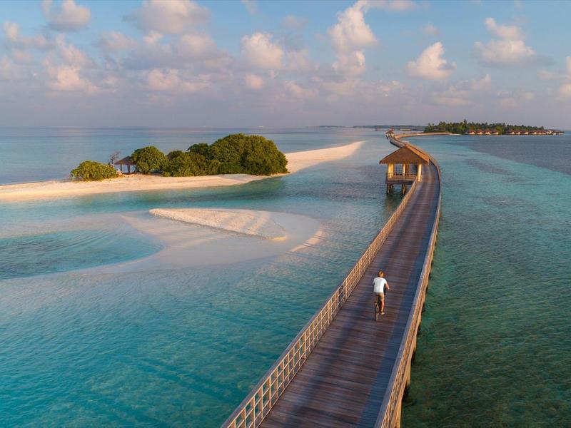 Langer Steg führt über türkisfarbenes Wasser zu kleinen, grünen Inseln unter blauem Himmel mit weißen Wolken.