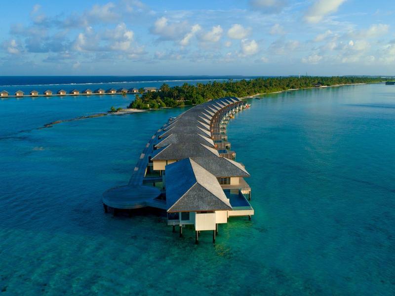 Lange Stege mit weißen Häusern führen über türkisblaues Meer zur kleinen grünen Insel.