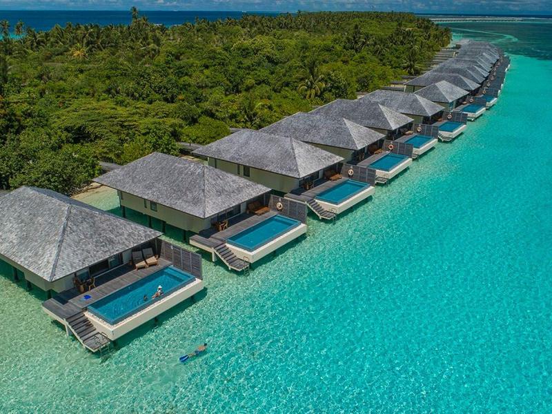 Reihe von Bungalows mit Pools über türkisblauem Wasser nahe einer grünen Insel.