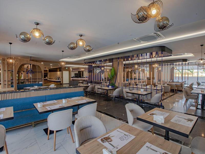 Moderner Restaurantraum mit blauen Sitzbänken, weißen Stühlen und dekorativer Deckenbeleuchtung.