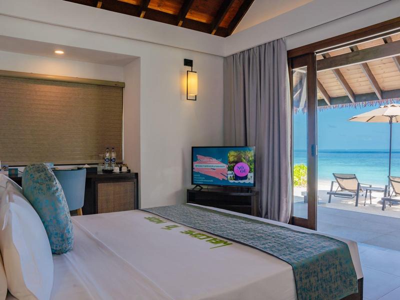 Helles Schlafzimmer mit großem Bett, Fernseher und offener Tür zur Terrasse mit Pool und Liegestühlen.