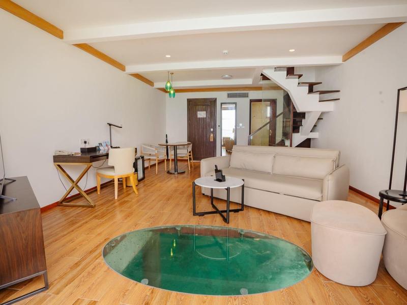 Wohnzimmer mit weißer Couch, Glastisch, Holzfußboden und moderner Treppe im Hintergrund.