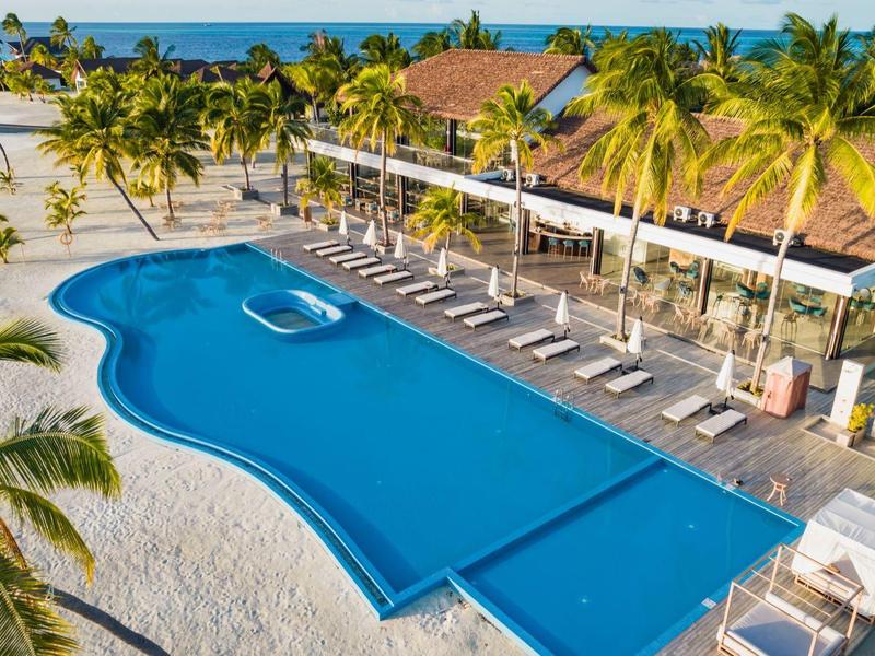 Hotelpool mit Liegestühlen und Palmen an einem tropischen Strand