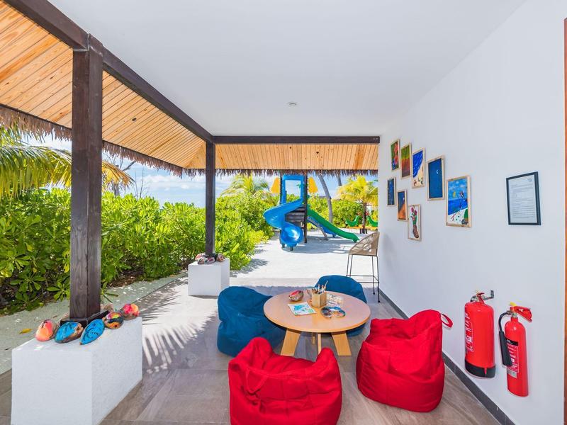 Überdachte Terrasse mit roter Sitzsäcke, runden Tisch, blauen Stühlen und Blick auf Garten mit Rutsche.