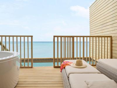 Blick von einer Terrasse mit Whirlpool und Liegen auf das Meer bei klarem Himmel.