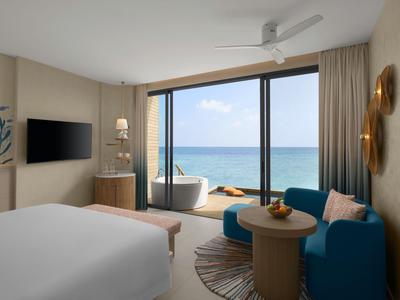 Modernes Hotelzimmer mit Bett, Sofa und Balkon mit Meerblick und Badewanne.