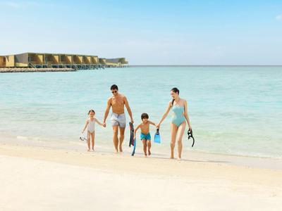 Rodzina z dwójką dzieci spacerująca po plaży, morze i niebo w tle.