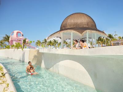 Luxe zwembad met mensen en opvallende koepelarchitectuur op de achtergrond bij heldere lucht.