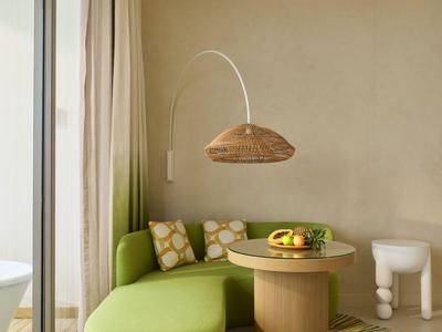 Modern eingerichtete Sitzecke mit grünem Sofa, rundem Holztisch und Stehlampe neben einer Glaswand.