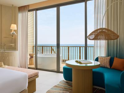 Modernes Hotelzimmer mit Meerblick, Couch, Tisch und Zugang zum Balkon mit Glasgeländer.
