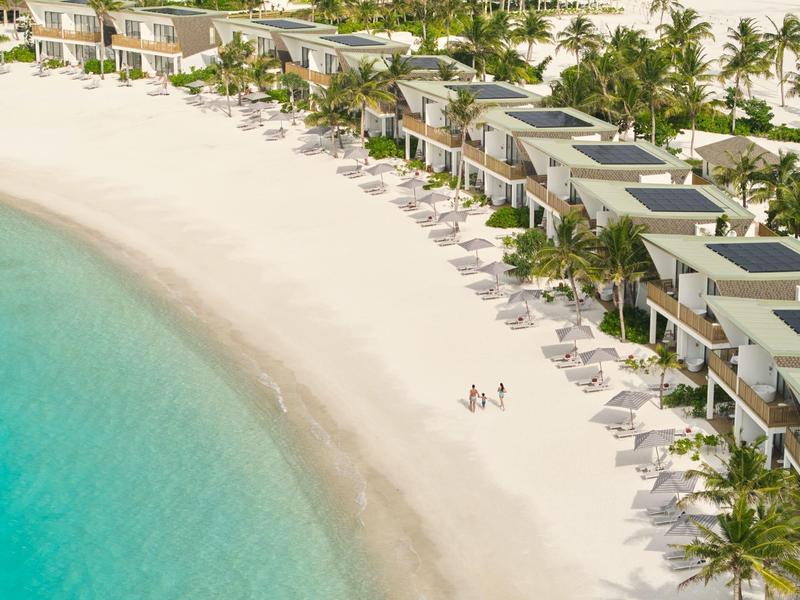 Uitzicht op strandvilla's met witte zandstranden en turquoise water, omgeven door palmbomen.