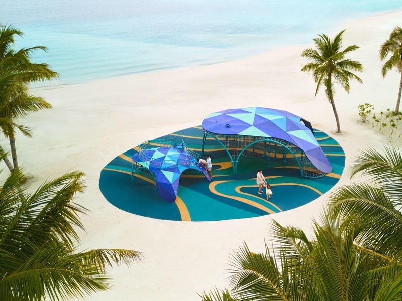 Moderne blauwe schaduwzeilen en zitplaatsen op een tropisch zandstrand met palmbomen.