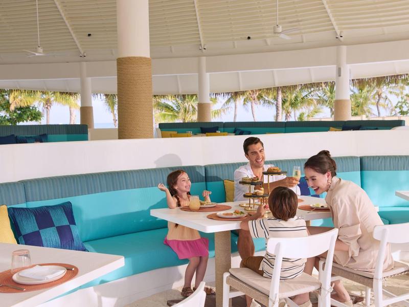 Familie geniet van een maaltijd in een helder, modern restaurant met turquoise zitbanken.