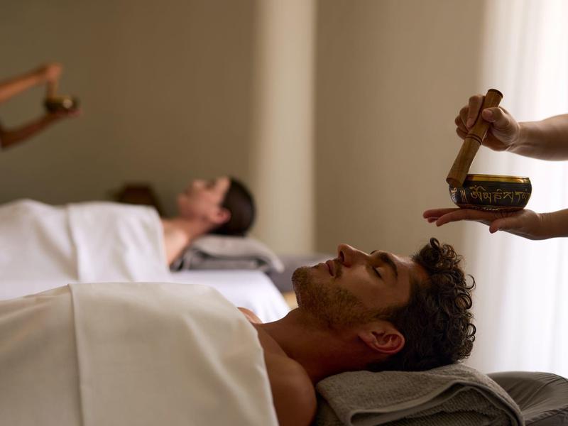 Een man ligt ontspannen onder een deken en krijgt een Ayurvedische behandeling met warme olie.