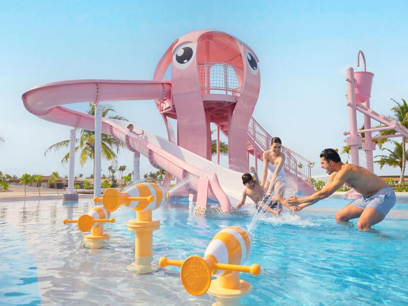 Kinderen spelen met ouders op een roze glijbaan in het ondiepe zwembad van een vakantieresort.