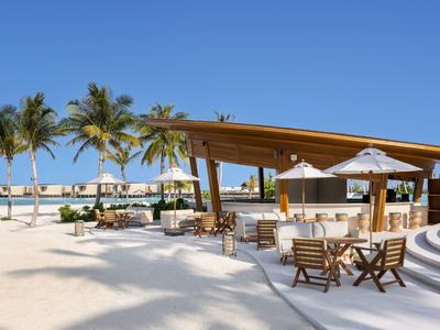 Bar de playa con palmeras, asientos y vista al mar bajo un cielo despejado.