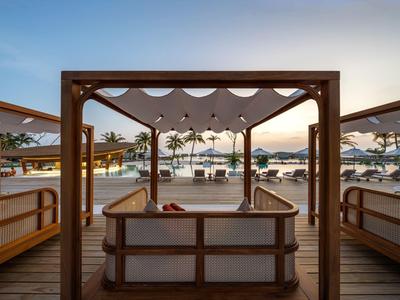 Lounge abierta con muebles de madera en un resort de playa al atardecer.