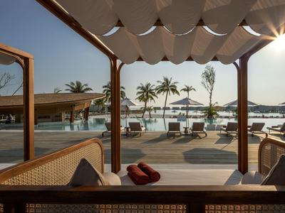 View of a hotel terrace with seating areas, sunshades, and palm trees on the beach at sunset.