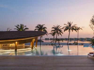 Zona de piscina al atardecer con palmeras y tumbonas junto al agua