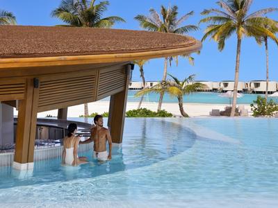 Bar en la piscina de un resort tropical con palmeras y vista al océano.
