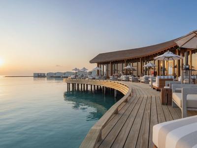 Muelle de madera con zona lounge y sombrillas sobre mar tranquilo al atardecer