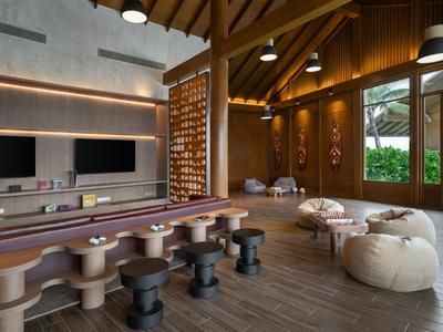 Área de salón moderna en hotel con taburetes y pufs cómodos bajo vigas de madera.