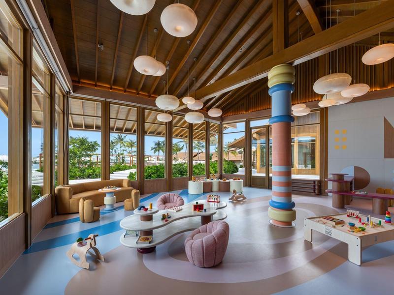 Sala moderna y luminosa con grandes ventanas, muebles coloridos y luces redondas.