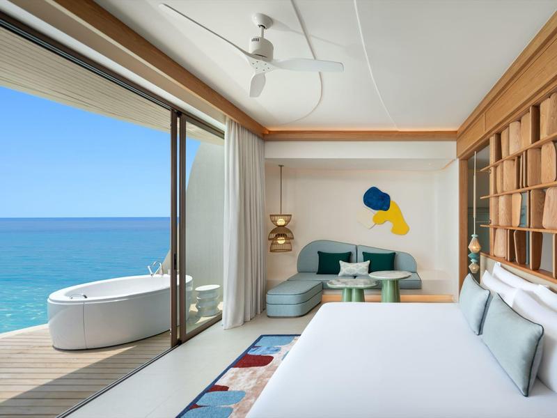 Habitación de hotel moderna con vista al mar, balcón abierto y bañera independiente.