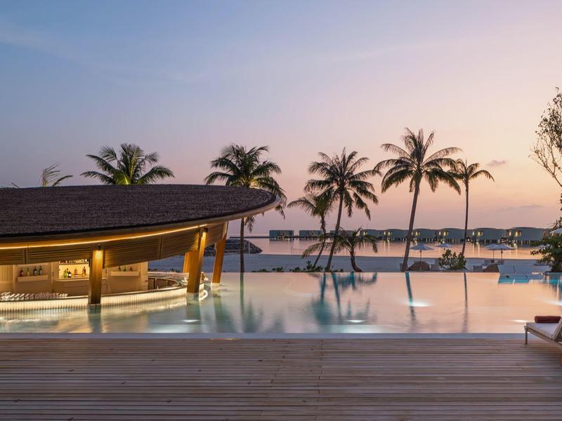 Zona de piscina al atardecer con palmeras y tumbonas junto al agua