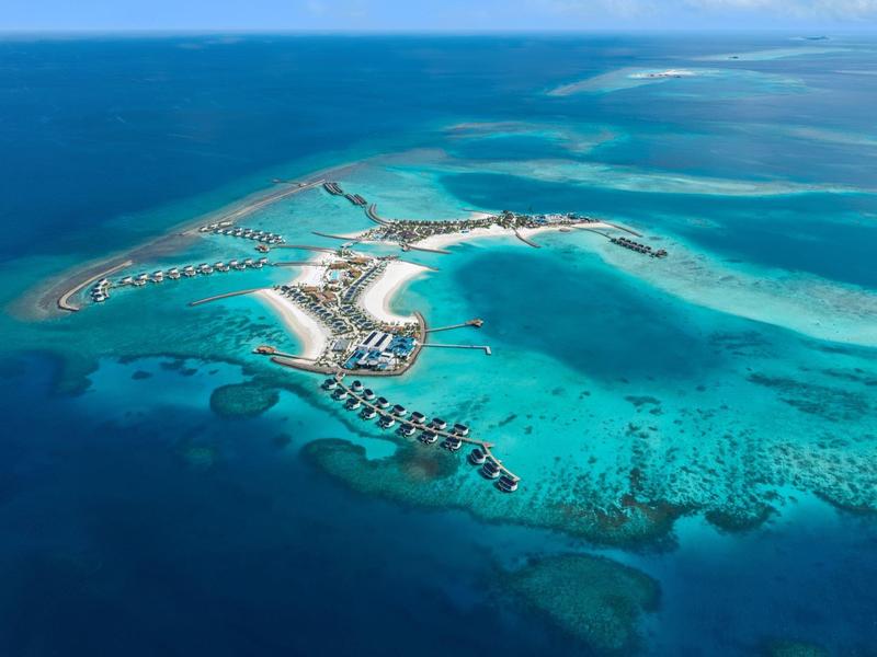 Vista aérea de una isla tropical con bungalows sobre el agua y mar turquesa claro