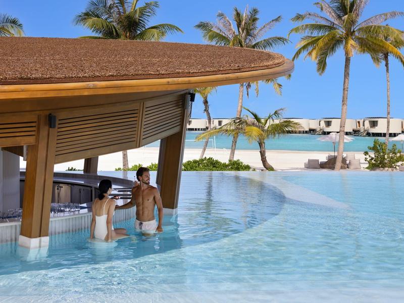 Bar en la piscina de un resort tropical con palmeras y vista al océano.