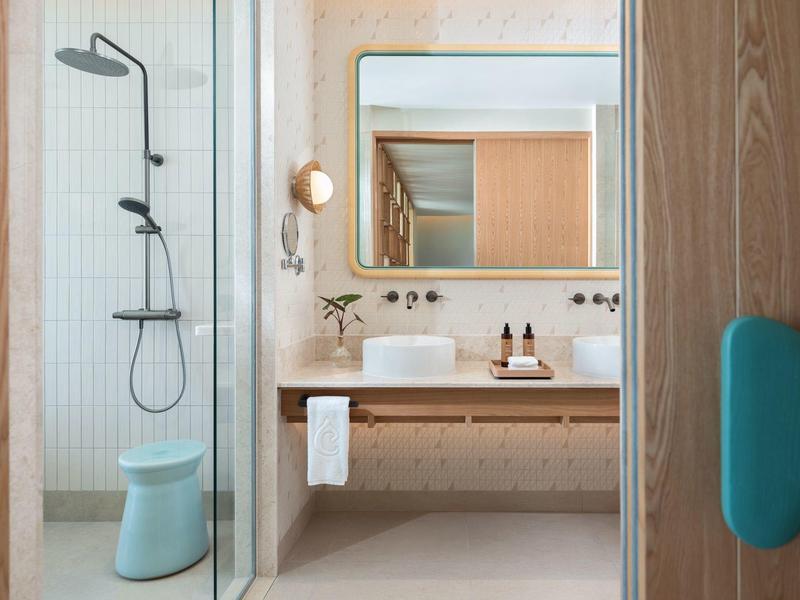 Baño moderno en hotel con ducha, estante de madera, toalla y espejo.