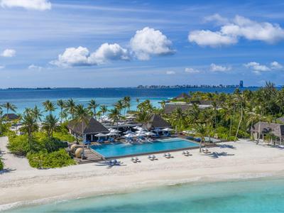 Resort de playa de lujo con piscina, palmeras y playa de arena blanca junto al mar turquesa.