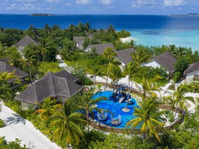 Tropical resort with pool surrounded by palm trees and bungalows by the sea.