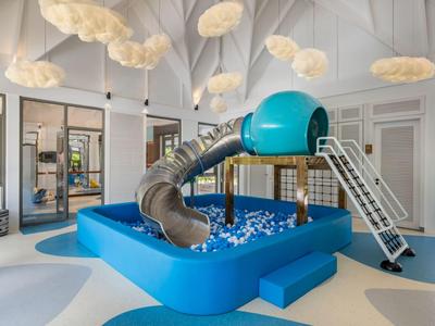 Indoor hotel area with blue ball pit and slide, surrounded by windows and ceiling lights.