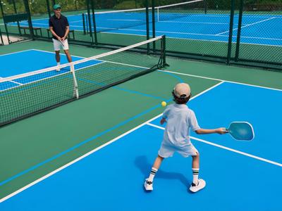 Two people playing pickleball on an outdoor tennis court with blue and green surfaces.