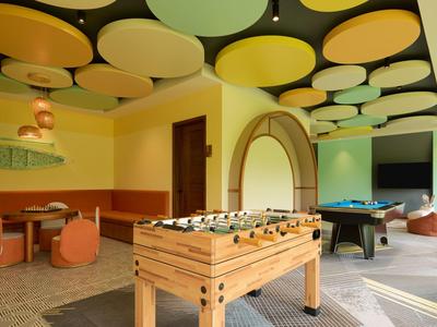 Modern game room with foosball, pool table, and colorful ceiling decorations in warm tones.