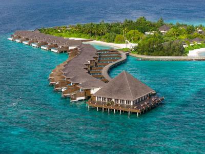 Overwater bungalows with pyramid-shaped roofs line a tropical island in clear blue sea.