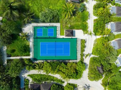 Aerial view of a tennis court surrounded by greenery next to a hotel or resort area.